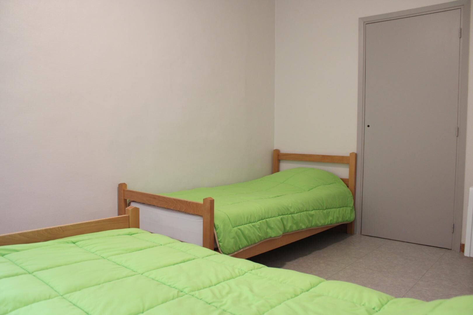 A small, single-bed room with a wooden frame and green bedding.