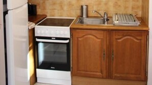 A compact kitchen with a white stove, wooden cabinets, a sink, and a hanging light fixture.