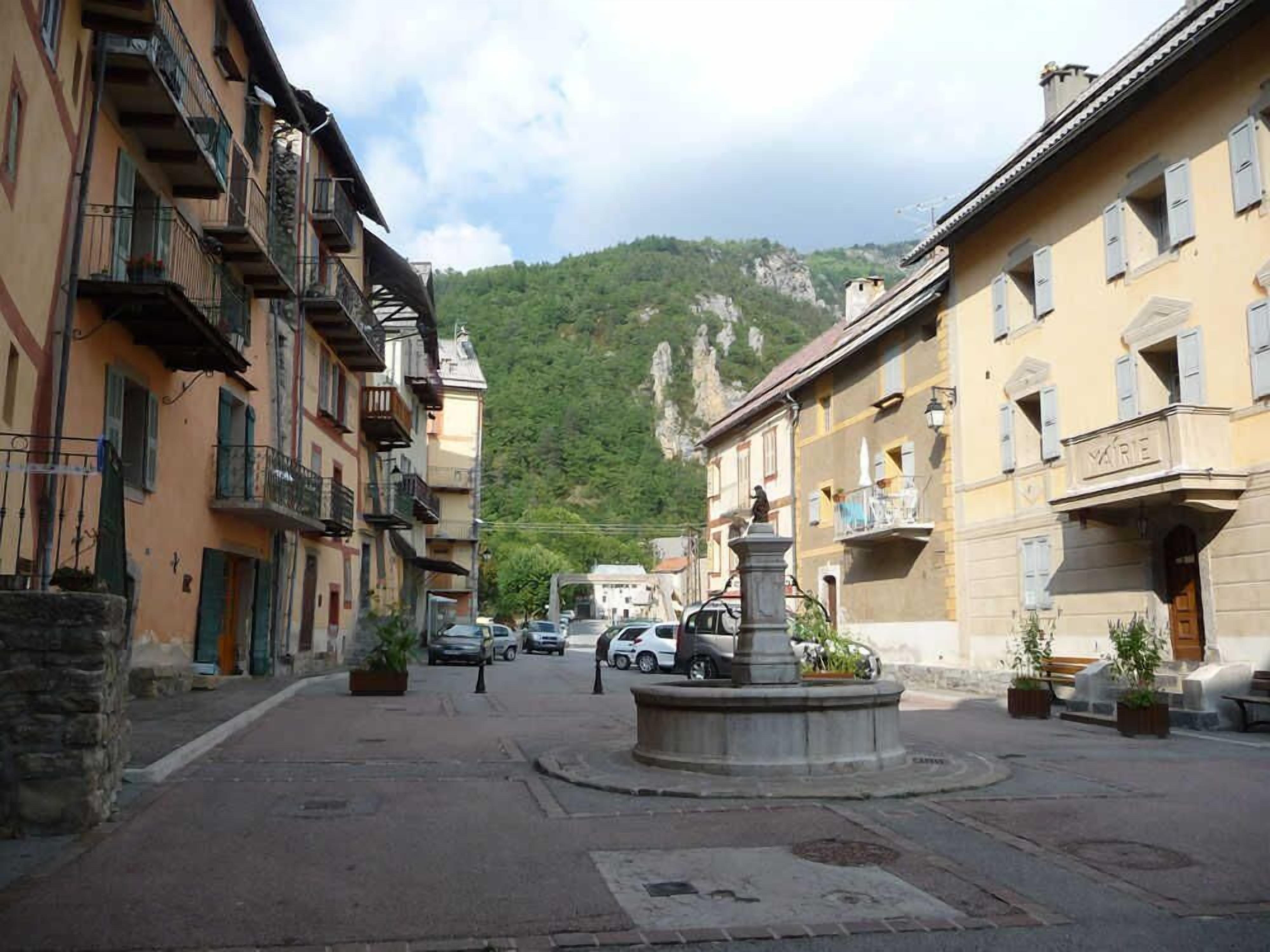 A street with buildings, a fountain, and a mountain in the background.