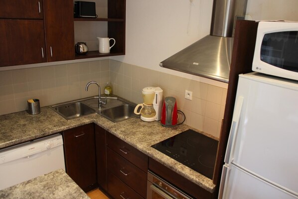 A kitchen with a dishwasher, double sink, microwave, and a stovetop.