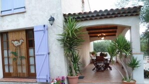 A patio area with a table and chairs, surrounded by potted plants and a wooden door with a towel hanging.