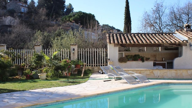 A swimming pool with lounge chairs, a tiled deck, and a garden with potted plants.
