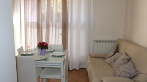 A dining area with a table set for two, a white sofa, and a window with sheer curtains.