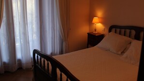 A bedroom with a bed, a nightstand with a lamp, and sheer curtains.