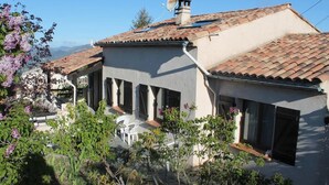 A two-story house with a tiled roof, satellite dish, and a garden with flowering plants.
