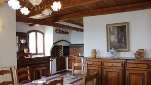 A dining area with wooden furniture, a table set for four, and a kitchen in the background with hanging pots.