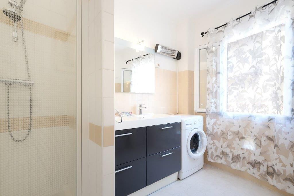 Une salle de bain moderne équipée d’un lave-linge, d’un miroir et d’une cabine de douche.