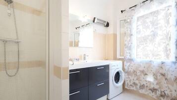 Une salle de bain moderne équipée d’un lave-linge, d’un miroir et d’une cabine de douche.