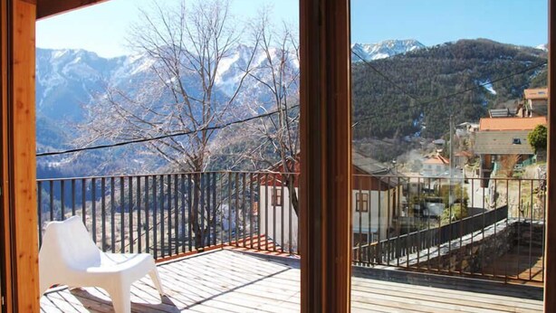 A wooden deck with a white plastic chair, a metal railing, and a view of snow-capped mountains and a village below. - La Grange du Lavoir - VENANSON (VENANSON)