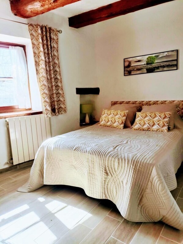 A bedroom with a large bed, a window with curtains, a radiator, and a wall-mounted lamp.