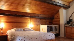 Et hyggeligt soveværelse med træloft, seng med mønstret dyne, sengeborde med lamper og en vugge.