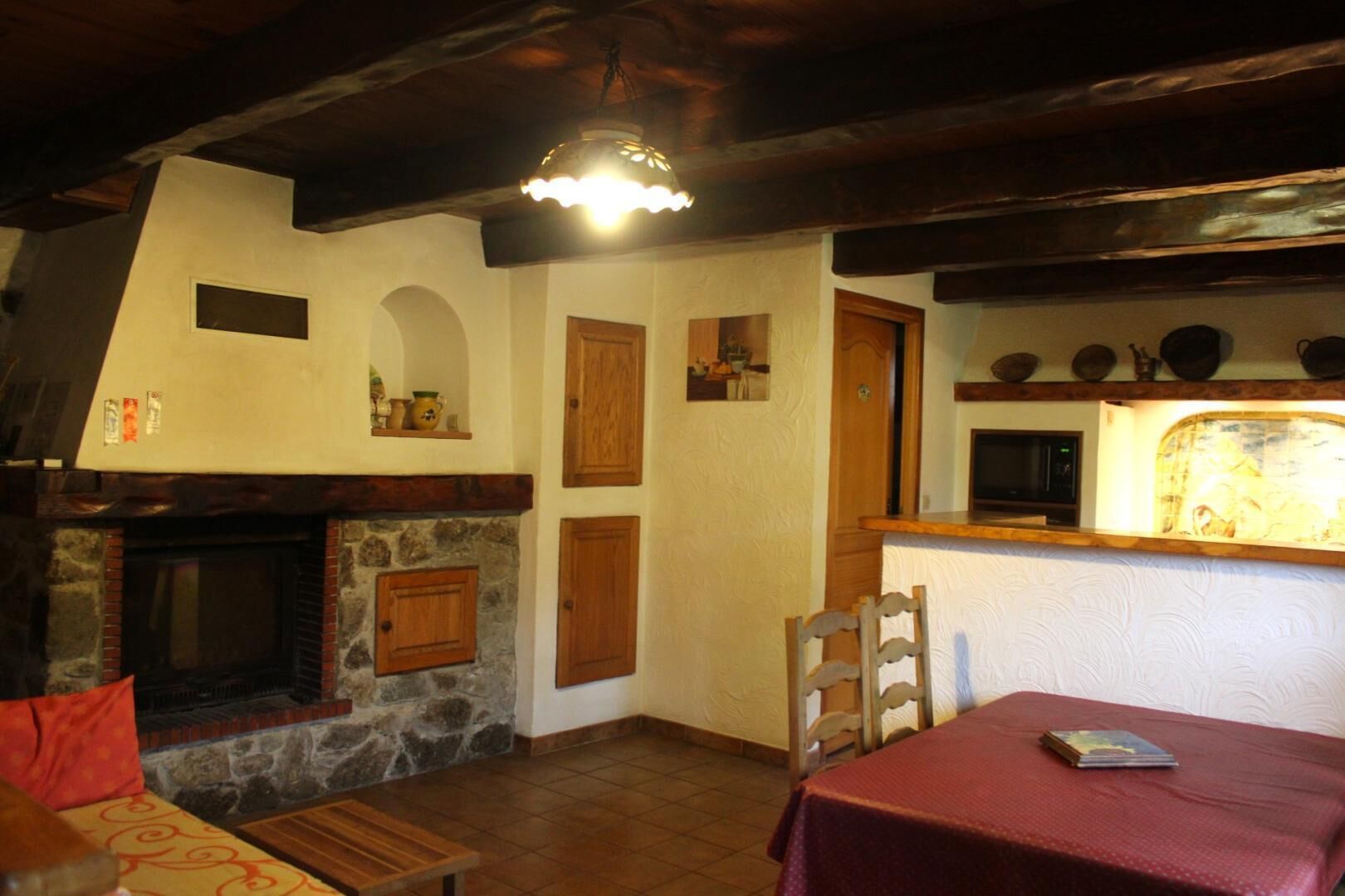Una habitación acogedora con chimenea de piedra, puertas de madera y una pequeña mesa con mantel rojo.