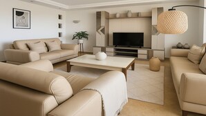 A modern living room with a beige sofa set, a coffee table, a flat-screen TV, and decorative vases. - Spacieux Appartement à Hydra (Timokten)