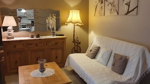 Een gezellige woonkamer met een houten salontafel, een witte bank met kussens, een lamp en een spiegel boven de kapstok.