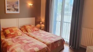 Een slaapkamer met twee bedden, een nachtkastje met een lamp, een raam met gordijnen en een schilderij aan de muur.