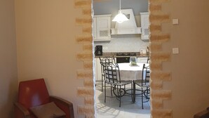 Een kamer met een eethoek, een rode stoel en een keuken zichtbaar door een open deur.