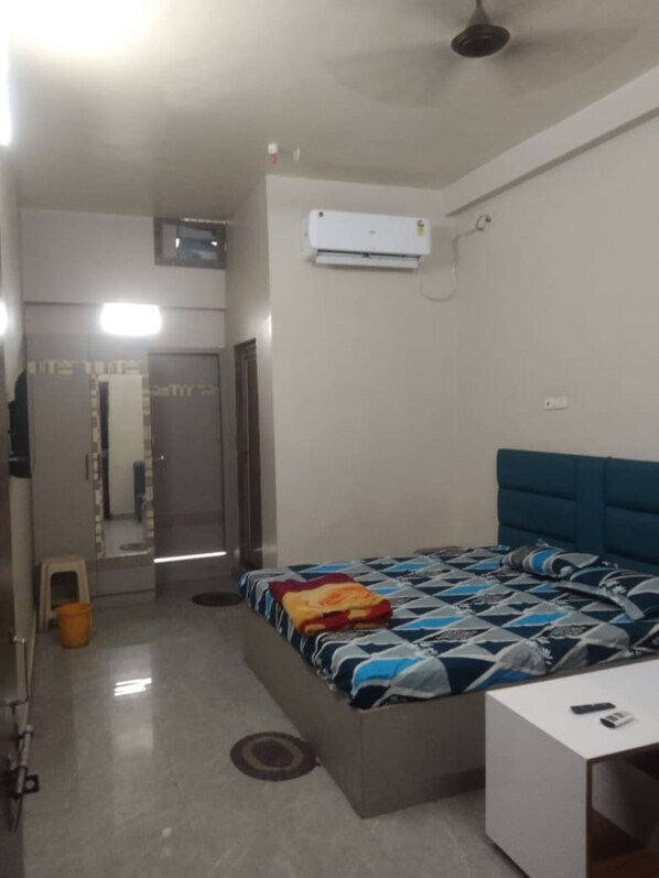 A bedroom with a bed, bedside table, air conditioning unit, and a mirror. - Hotel Muskan (Raipur)