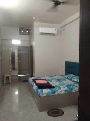 Un dormitorio con cama, ventilador de techo, equipo de aire acondicionado y un taburete pequeño.
