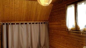 A room with wooden walls and a sloped ceiling. There is a window with curtains and a hanging light fixture.