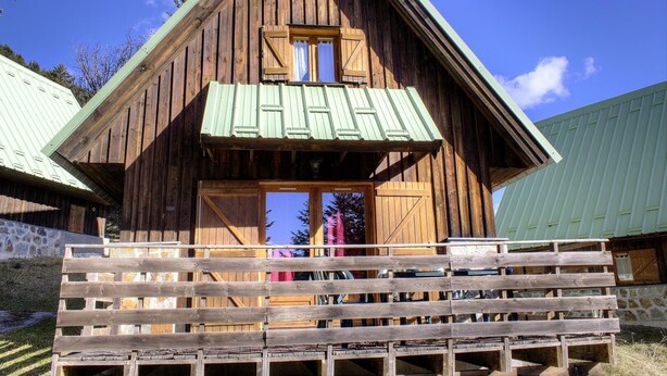 A wooden cabin with a sloped roof, a balcony, and a large window.