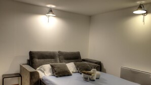A single bed with a grey headboard and pillows, a small bedside table, and two wall-mounted lights.