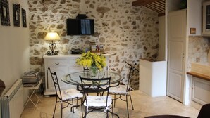 Un coin repas avec un mur en pierre, un téléviseur fixé au-dessus d’un meuble blanc et une table avec des chaises.