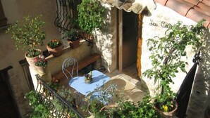 Un petit espace extérieur aménagé avec une table et des chaises, entouré de plantes en pot et d’un mur de pierres.