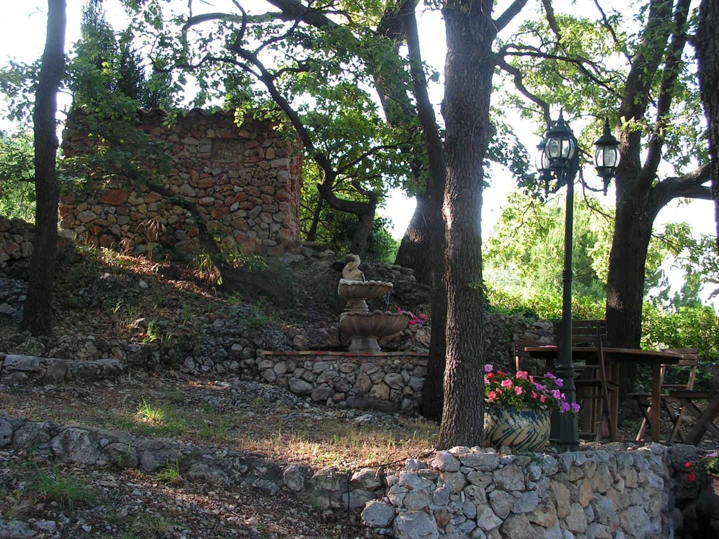 A stone wall, a bird bath, and a wooden bench in a garden setting.