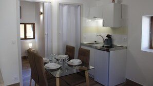 A compact kitchen with white cabinets, a sink, and a small dining area with a glass table and chairs.