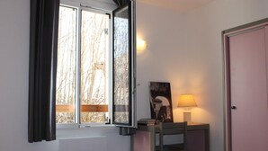 A room with a bed, a desk with a lamp, a window with curtains, and a door.