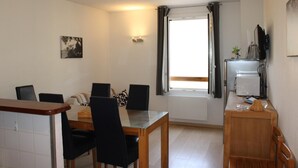 A compact living space with a dining area, kitchenette, and a large window with curtains.