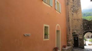 Une rue étroite bordée d’un bâtiment dont les portes sont surmontées d’arcs et qui présente une arche en pierre.