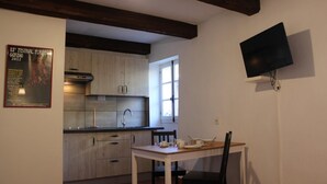Une cuisine avec des meubles de rangement en bois, un évier et un coin repas comprenant une table et des chaises. Un téléviseur à écran plat est fixé au mur.