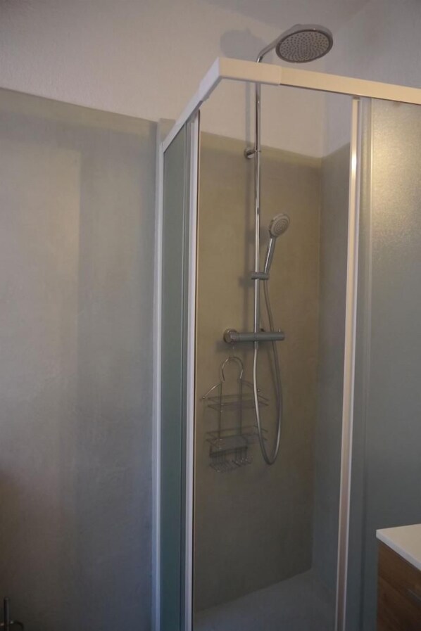 A glass-enclosed shower with a handheld showerhead and a wall-mounted faucet.