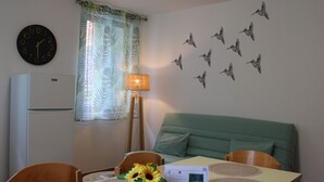 A room with a bed, a table with a vase of sunflowers, a clock, a lamp, and wall decals of birds.