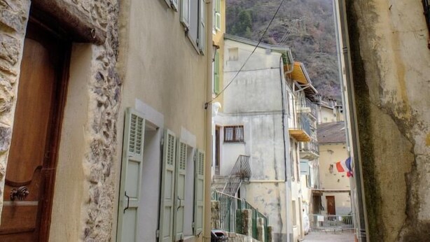 A narrow street with stone buildings, wooden doors, and shutters.