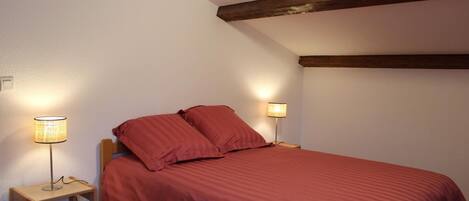 A bedroom with a single bed, two bedside lamps, and a wooden ceiling beam.
