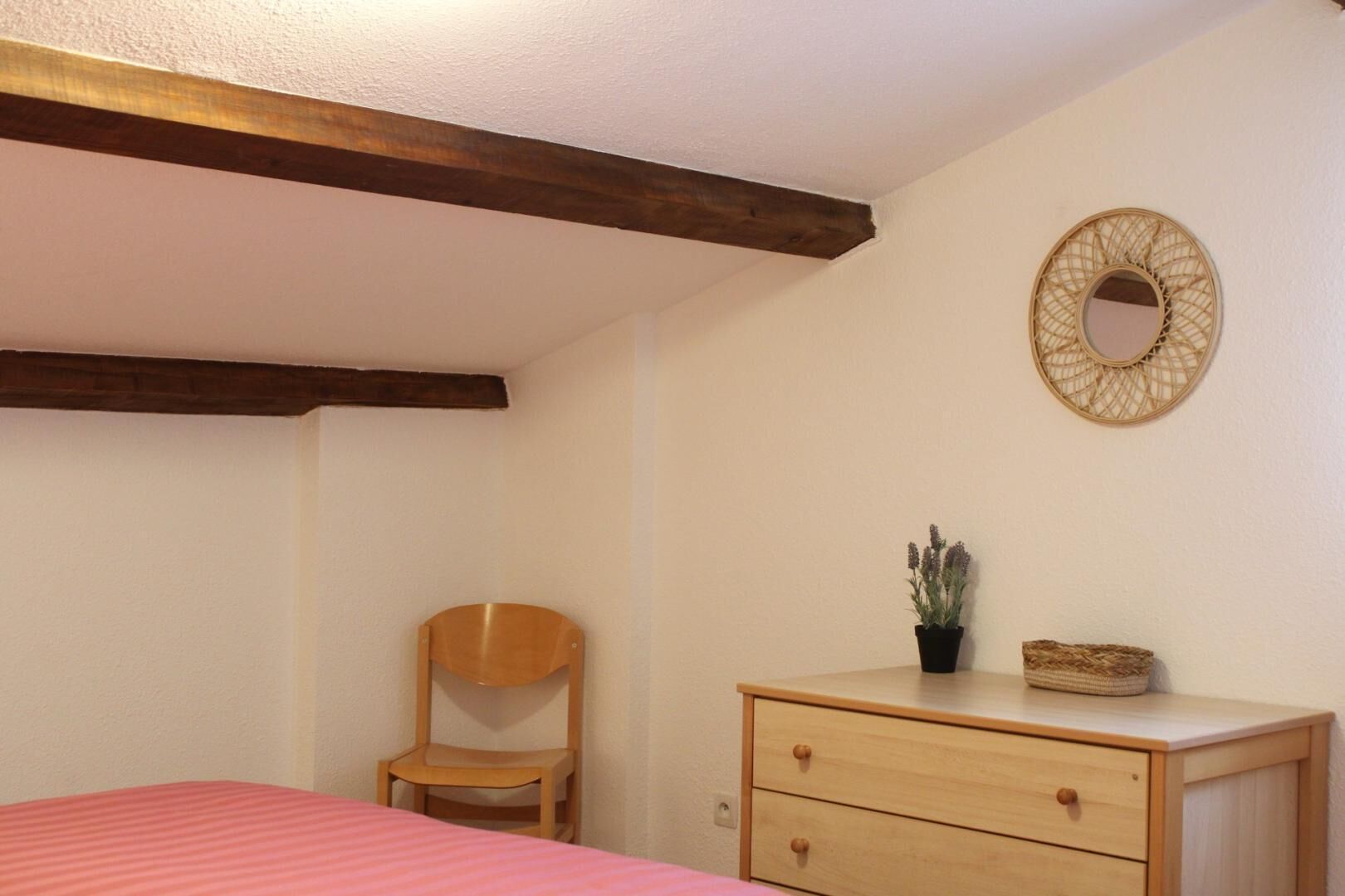 Une chambre à coucher comprenant un lit, une chaise en bois, une commode et un miroir fixé au mur.