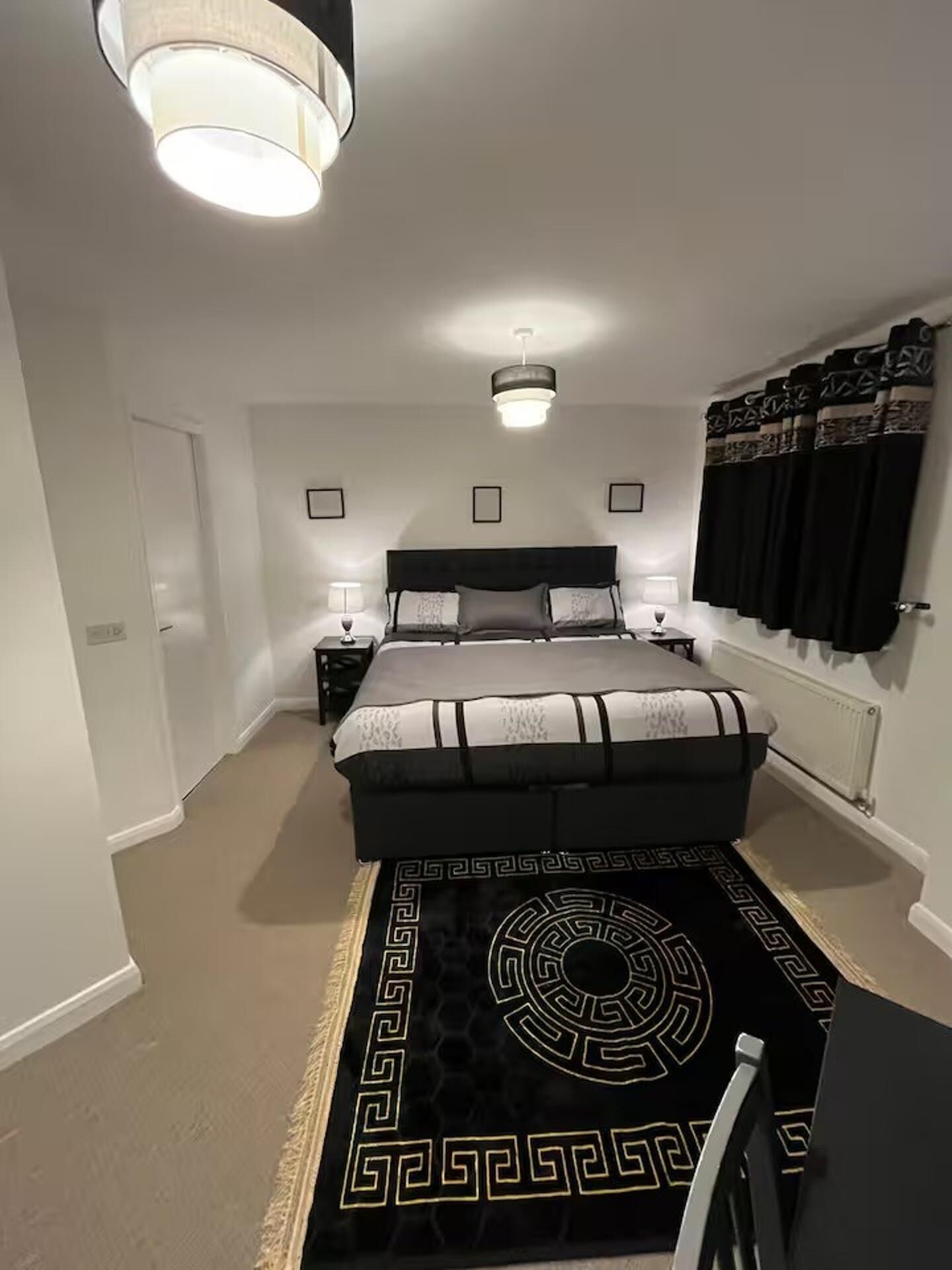 Une chambre à coucher avec un grand lit, deux tables de chevet, un tapis à motifs géométriques et un luminaire au plafond.