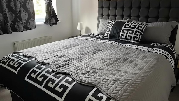 A neatly made bed with a patterned bedspread and pillows, a tufted headboard, and a window with curtains. - Central 2-bed Apartment - Sleeps 5 & Free Parking (Derby)
