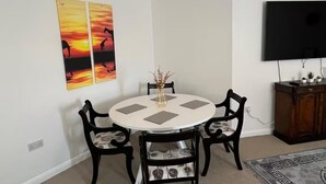 A dining area with a round table, four chairs, a vase with dried flowers, and a flat-screen TV mounted on the wall. - Central 2-bed Apartment - Sleeps 5 & Free Parking (Derby)