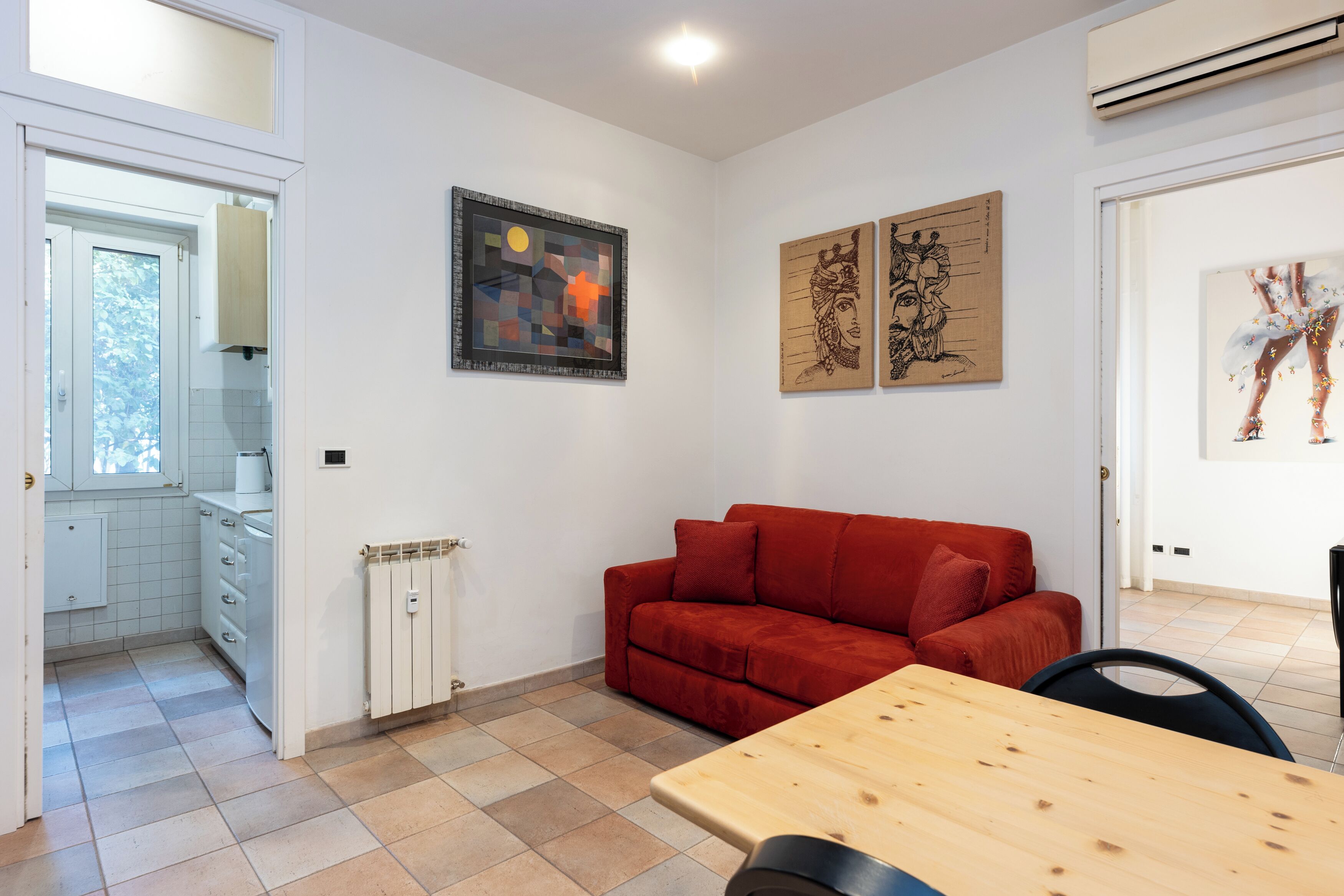 Una sala de estar moderna con un sofá rojo, una mesa de madera y obras de arte en las paredes.