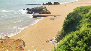Una playa con afloramientos rocosos, una orilla arenosa y vegetación.