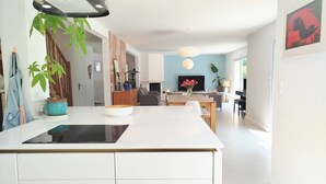 Una cocina moderna con una isla central, un área de comedor con un sofá y una sala de estar con televisor.