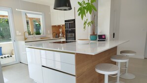 Una cocina moderna con armarios blancos, una isla central con taburetes, horno integrado y un amplio ventanal.
