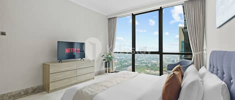 Habitación de hotel moderna con una cama grande, un televisor mostrando Netflix, una vista de la ciudad a través de amplios ventanales y un paisaje urbano en el exterior.