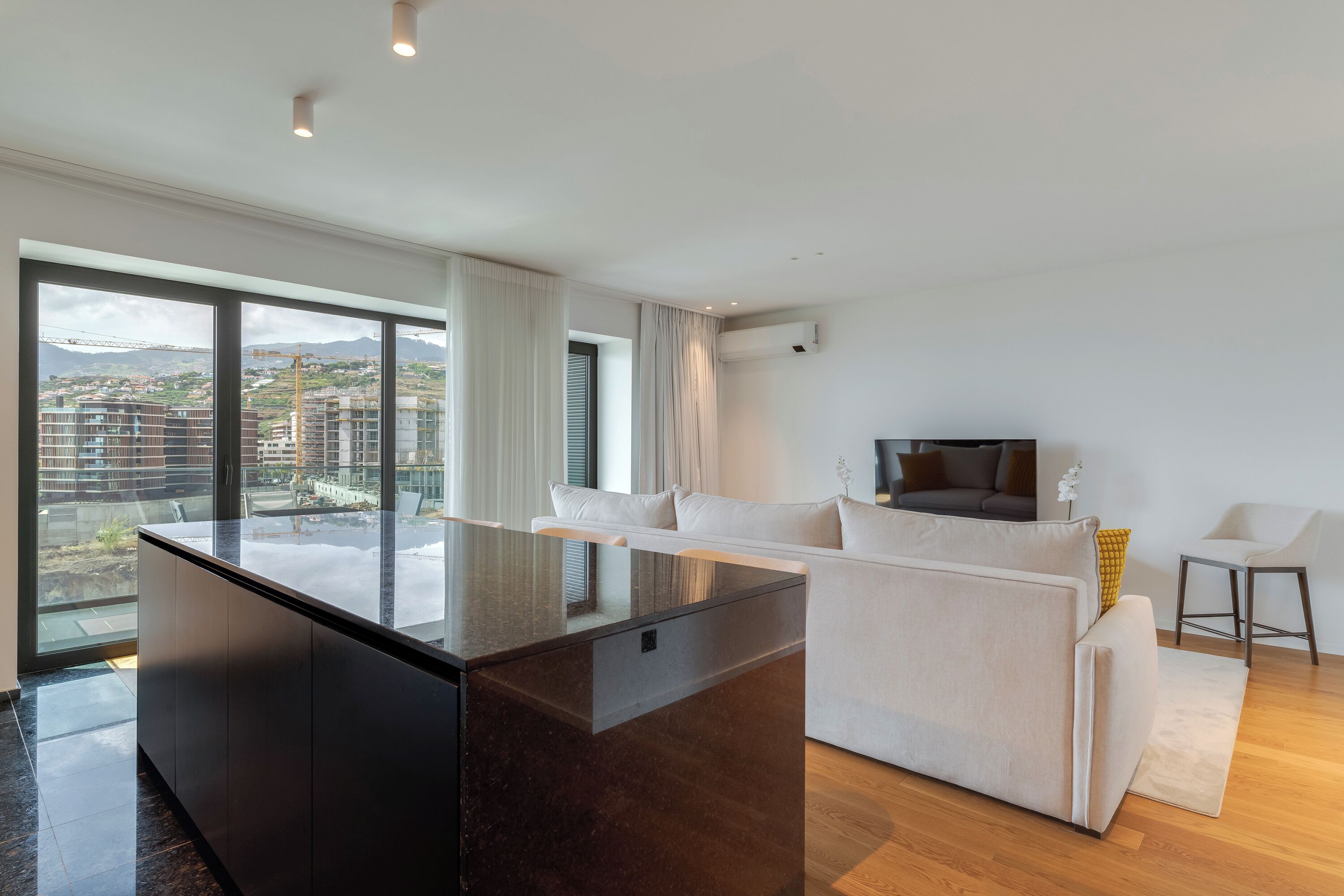 A modern living room with a large window, a sofa, a TV, and a small table.