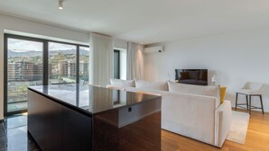 A modern living room with a large window, a sofa, a TV, and a small table. - Oceanview Pearl Apartment (Funchal)