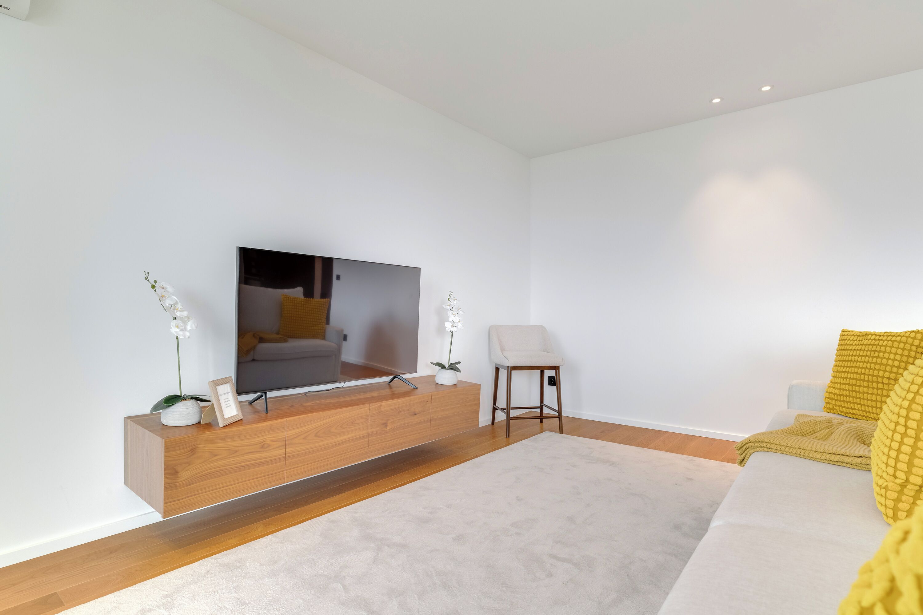 Ein modernes Wohnzimmer mit einem Holztischchen, einem Flachbildfernseher, einer Couch und einem Sessel.