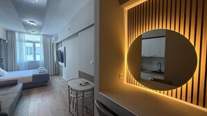 A modern hotel room with a bed, a small table, a TV, and a wall-mounted mirror reflecting a kitchen area. - Monastiraki 303 Superhost Hub (Athens)